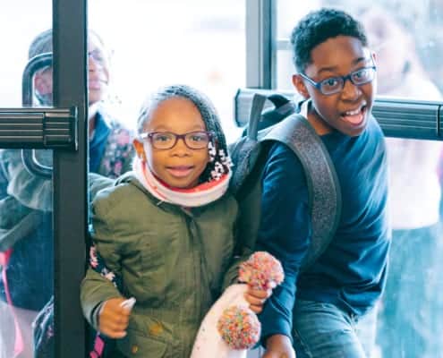 Two children in winter coats coming through doors of Club