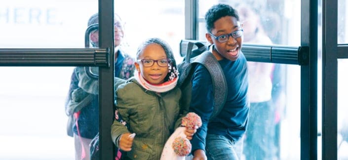 Two children in winter coats coming through doors of Club