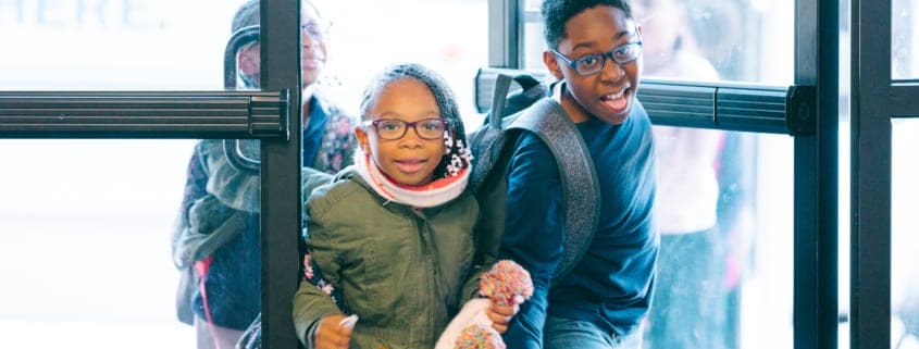 Two children in winter coats coming through doors of Club