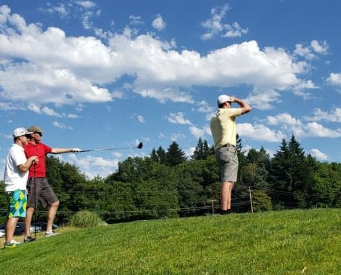 Three golfers gaze out at course against a blue sky with scenic clouds, one points with club