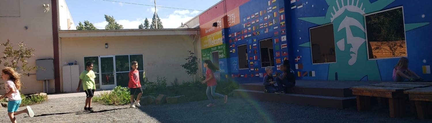Kids run through inukai play space with entry doors and the rainbow-hued mural in the background.