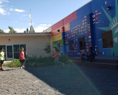 Kids run through inukai play space with entry doors and the rainbow-hued mural in the background.