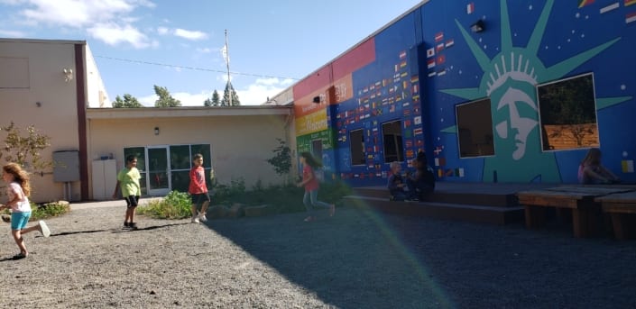Kids run through inukai play space with entry doors and the rainbow-hued mural in the background.