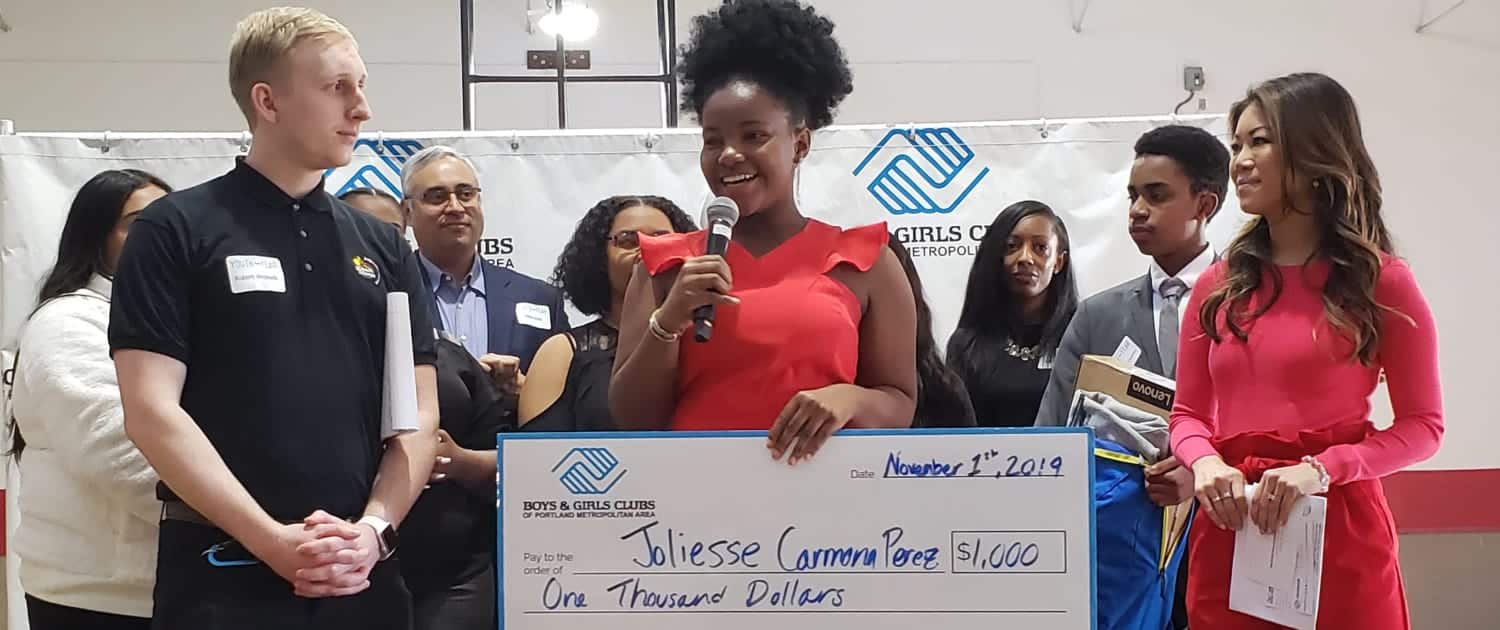 Joliesse Carmona Perez on stage giving speech with scholarship check immediately after she was announced as the Portland Metro Youth of the Year by judges on stage behind her..