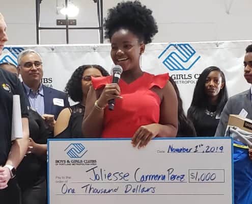 Joliesse Carmona Perez on stage giving speech with scholarship check immediately after she was announced as the Portland Metro Youth of the Year by judges on stage behind her..
