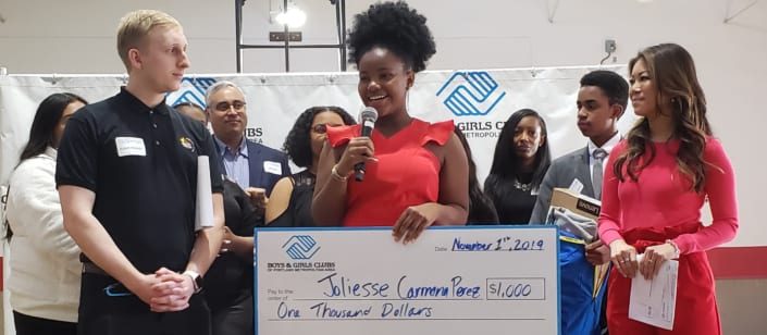 Joliesse Carmona Perez on stage giving speech with scholarship check immediately after she was announced as the Portland Metro Youth of the Year by judges on stage behind her..
