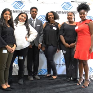 Youth of the Year Candidates stand in a group against the Boys & Girls Clubs branded backdrop on the stage.