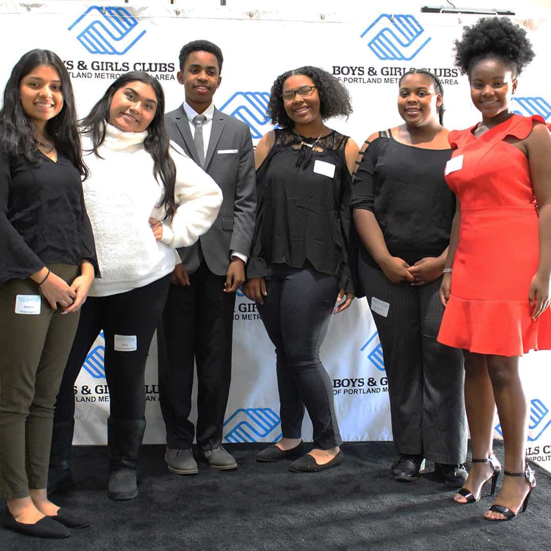 Youth of the Year Candidates stand in a group against the Boys & Girls Clubs branded backdrop on the stage.
